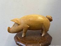 Front side view of whimsical carved wooden pig sculpture on wooden stand.