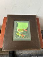 Front view of the framed painting showing the red-eyed tree frog artwork and signature.