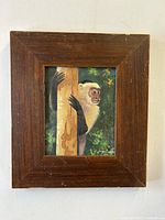 Front view of the wood framed painting of a white-faced capuchin monkey.