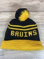 Photograph of a black knit winter hat with yellow stripes, yellow 'BRUINS' text, yellow cuff, and yellow/black pom pom on wood background.