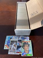 Open box view showing large number of Topps baseball cards from 1978-1985 stacked inside a long box with some cards laid out in front including an A.L. All-Star Rod Carew card and others.