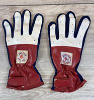 Pair of 1980s Boston Red Sox left handed child size large souvenir batting gloves shown palm side up on wood surface. Gloves have red wrist cuff with Boston Red Sox logo patches and ventilation holes on the white fingers and back hand panel. Navy blue trim edging visible.