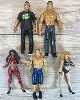 Photo showing all 5 WWE wrestling action figures including John Cena and Bautista along with three female wrestlers, posed on wooden floor.