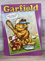 Front cover of the 1980s Mead Garfield portfolio folder showing Garfield with a baseball bat and teddy bear catcher