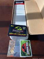 Wide view of a large cardboard box filled with Jurassic Park trading cards, showing the front card with dinosaur artwork and Jurassic Park packaging.