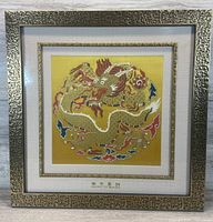 Square gold framed woven textile showcasing a traditional Chinese dragon against a yellow background, with intricate embroidery detailing.
