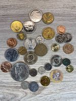 Overhead photo showing 33 assorted coins of different sizes, designs, materials, and countries of origin laid on a light wooden surface.