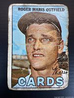 Front side of the baseball card with a color photograph of Roger Maris in an outfield baseball cap and uniform, labeled 'Roger Maris Outfield Cards'. Card is heavily creased and worn along edges and surface.