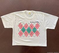 Front view of a white vintage 1980s single stitch crop top T-shirt with Boston College embroidery and pink and green argyle pattern.