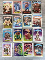 Top-down photo showing 17 Garbage Pail Kids collectible cards arranged in four rows on a wooden surface. Each card depicts a unique cartoon character with vibrant colors and varied designs.