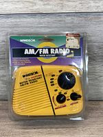Yellow Windsor brand AM/FM water resistant radio in sealed original packaging, showing front panel with dials and speaker grille.
