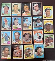 Photo shows 18 vintage baseball cards arranged in rows on a dark surface. Cards depict mid-20th century baseball players with varied colored backgrounds and team logos.