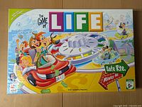 Front of the Game of LIFE Family Edition box showing colorful cartoon characters and the game spinner in the center