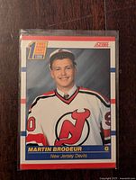 Front side image of 1990-91 Score Martin Brodeur rookie card showing player in New Jersey Devils jersey with first round draft pick logo.