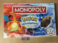 Front of Pokemon Monopoly box featuring Charizard and Blastoise with title and 6 metal tokens indicated.