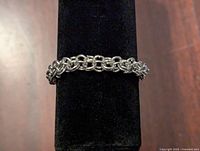 Close-up photo of the silver tone chain link bracelet displayed on a black stand, showing the interlocking links and clasp.