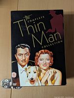 Front cover of The Thin Man Complete Collection DVD box set featuring illustrated portraits of the main characters and a dog.