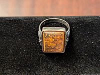 Front view of the ring showing the rectangular amber stone and silver-tone band with decorative details.