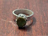 Top view of women's ring showing green jasper stone set in metal band on wooden surface.