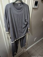 Full view of two-piece gray loungewear set hung on door, showing top and pants with light trim detailing.