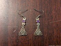 Front view of pair of silver-tone dangle earrings with purple round stone above Ontario Trillium flower charm on wooden surface
