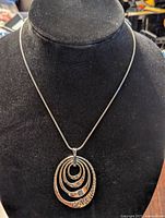 Front view of silver pendant necklace featuring four nested hammer-textured oval pendants on a chain displayed on a black velvet bust.