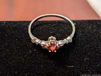 Front view of a sterling silver women's ring with heart-shaped red gemstone in the center and detailed band design.
