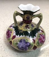 Photo of antique Nippon double-handled gilt beaded vase with purple and pink flowers and raised gold dots on green background, fluted white lip