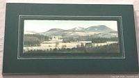 Framed artwork shown from the front, revealing a rural landscape with castle, trees, and mountains under a cloudy sky, bordered by silver edging and dark green matting.