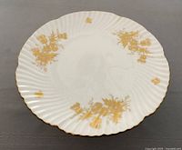 Top-down view of white bone china plate with gold floral decorations and gold rim on a gray surface.
