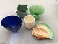 All five items displayed including blue opalescent vase, green aged finish vase, solid green ceramic vase, white raised fern vase, and leaf-shaped dish.