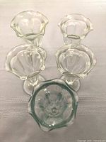 Top-down and angled view of five vintage glass ice cream sundae dishes showing the wavy fluted rims, various sizes, and clear glass panelled design.