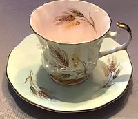 Tea cup and saucer with wheat sheaf design on mint green and pink with gold trim