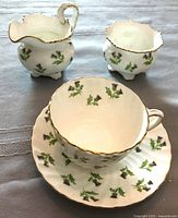 Tea cup, creamer, and sugar bowl set with green leaf pattern and gold trim on white bone china.