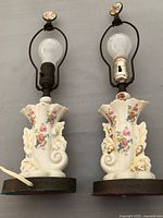 Photo showing both matching vintage boudoir lamps side by side, highlighting porcelain bases with floral designs, bulbs and metal frames with finials.