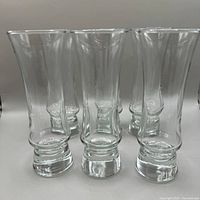 Front view of six clear glass parfait glasses with thick solid glass bases and flared tops, arranged together.