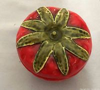 Top view of the strawberry jam jar lid featuring textured green leaves on a red base.