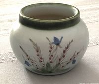 Side view of rounded stoneware jar showing blue bell flower and heather sprig hand painted decoration with dark green rim
