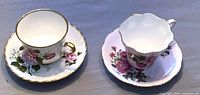 Photo showing both white and pink floral tea cup and saucer sets on a table, capturing overall appearance and scale.