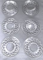 Top-down photo showing all five clear, round glass plates arranged in two rows. Each plate has a clear star cut pattern around the rim with a smooth center and raised base.