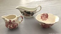 Three vintage dishware pieces including cream pitcher, sugar bowl, and small sauce dish with floral and transferware patterns