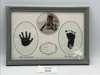 Photo of first baby handprint and footprint frame showing black ink prints, circular baby photo, and birth details label.
