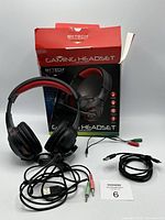 Black and red BYTECH gaming headset with attached cables and damaged box in background.