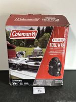 Photo of the original box showing Coleman branding, Fold N Go model, 20,000 BTU and two burner features, plus compact and folding design illustration.