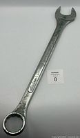 Full view of the large metal combination wrench with both open and box ends, showing general wear and size proportions.
