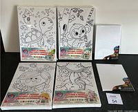 Five paint by number kits laid out on a floor with black and white cartoons, some showing sea turtle, monkey, various characters