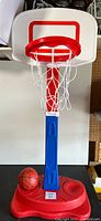 Full shot of the kids basketball hoop, showing red hoop with white net, blue support post, and red plastic base.