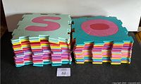 Two stacks of colorful alphabet foam floor tiles with interlocking edges shown from side front