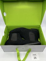 Pair of black Chelsea boots in green interior box, showing boots side profile and elastic side panel.
