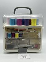Singer branded plastic sewing carrying case with clear cover and handle showing multiple spools of colored thread and sewing accessories inside organized in compartments and drawers.